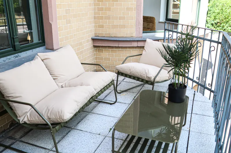 Balcony of the Bauhaus Suite with a lounge sofa, armchair, glass table and palm in the quiet courtyard