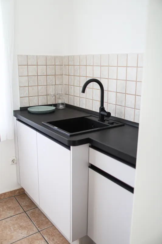 Kitchen sink with black tap, dark worktop and light tiled splashback