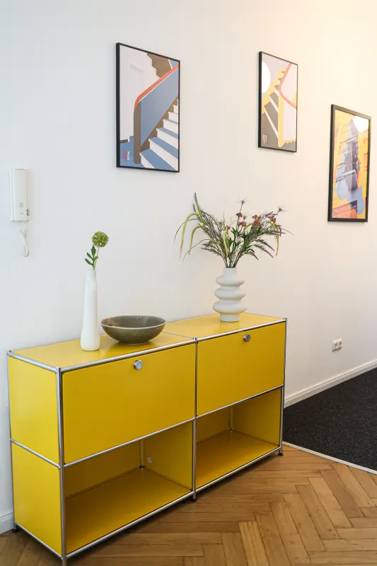 Yellow USM Haller sideboard with vases below three framed Bauhaus graphics on herringbone parquet