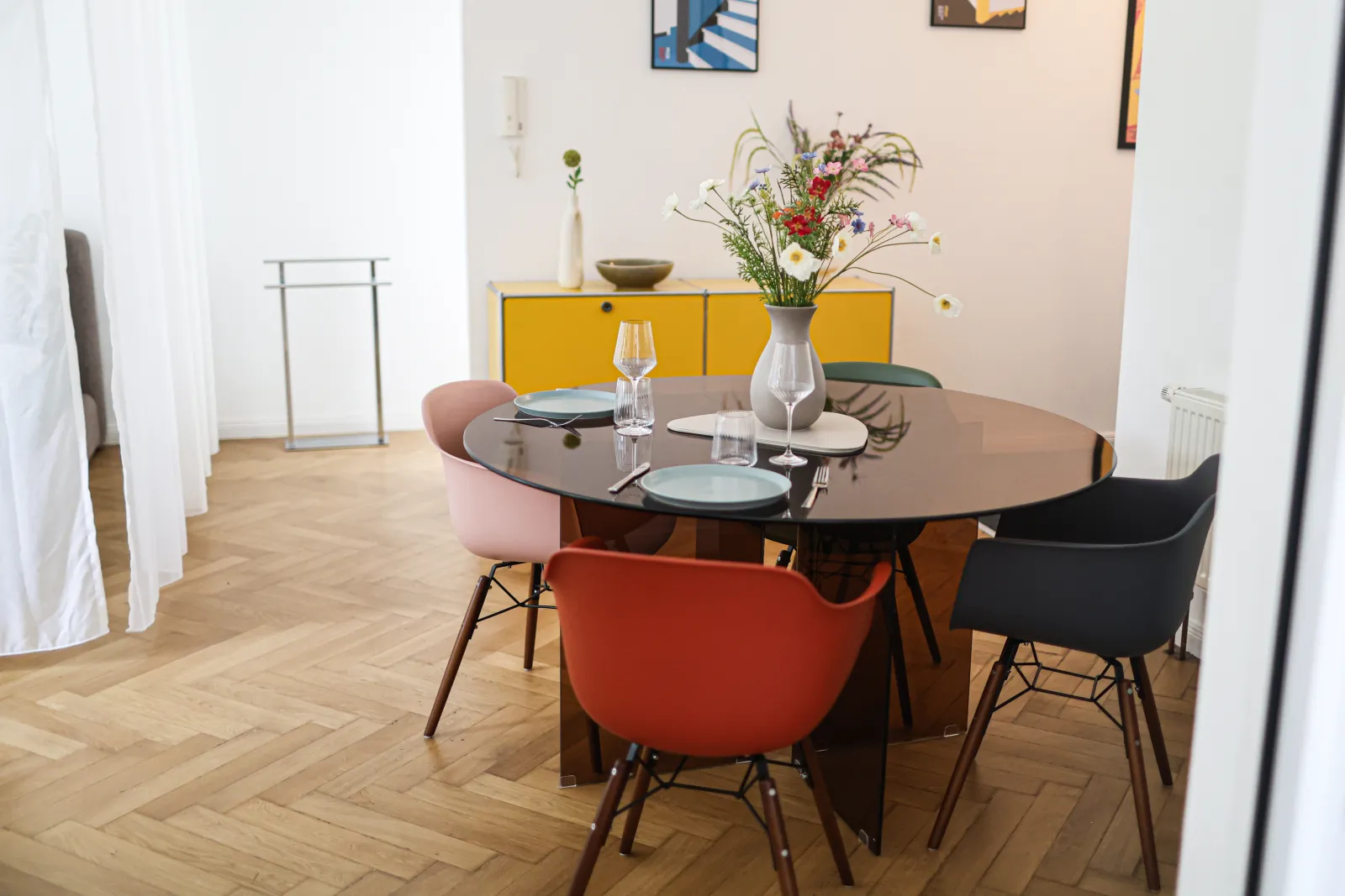 Bright living room of the Bauhaus Suite with a round dining table, Eames chairs, yellow USM sideboard and herringbone parquet