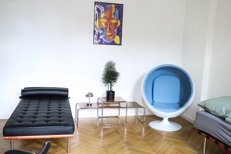 Second room with a black daybed, blue ball chair and chrome side tables on parquet flooring